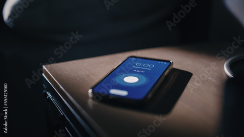 Smartphone Alarm Clock App Rings for Wake up, Screen Shows "Good Morning" and Time of Six in the Morning. Close-up Focus on Mobile Phone Ringing. Bedside Nightstand bedroom Apartment