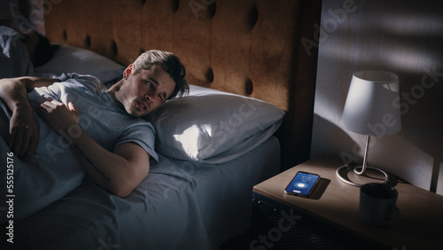 Man Wakes Up, Turns off Alarm Clock with Frustration, after Sleepless Insomniac Night. Stressed Man Ready to Face Day of Problem Solving. Focus on Clock Showing Eight A.M. bedroom Apartment