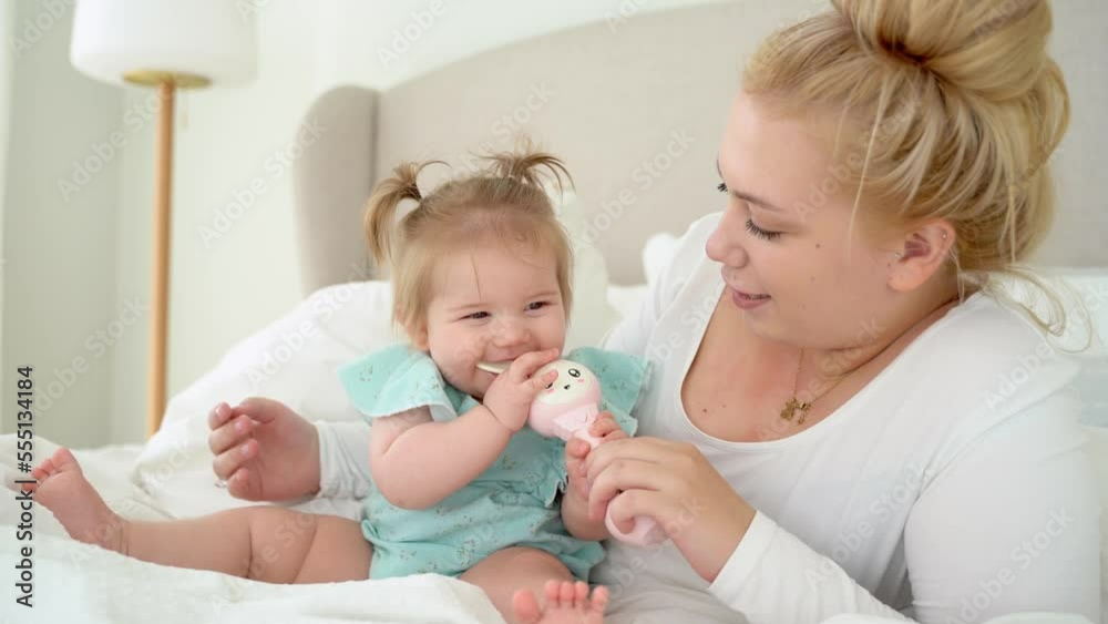 Mother plays with her baby daughter in bed in morning. Family grows child in love and care. Happy parent and child spent time together. Childhood, parenthood. Mother plays with her baby daughter in bed in morning. Family grows child in love and care. Happy parent and child spent time together. Childhood, parenthood.