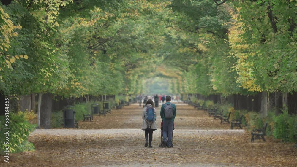 Young parents with child in baby buggy walking on the alley in the park during a beautiful autumn day Young parents with child in baby buggy walking on the alley in the park during a beautiful autumn day