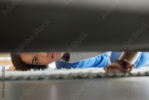 Woman, confused and couch looking for lost product in her home living room with doubt. Female, floor and checking under sofa for a missing item and searching her apartment or house in the carpet photo