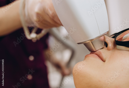Therapist beautician makes a laser treatment to young woman's face at beauty SPA clinic. Facial laser hair removal epilation procedures. Close up. photo