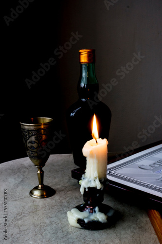 A burning candle on the table in front of a glass and a bottle. Soft focus