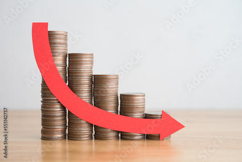 Stack of coins bar chart and red curve graph trending downwards with white wall background on wooden table copy space. Economy recession crisis, inflation, stagflation, business and financial loss. photo