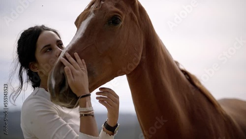 Pretty brunette woman loves her horse and kisses in the face, closeup video of girl and animal in the field as best friends