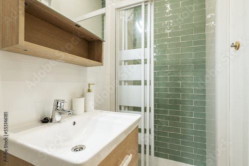 Bathroom with small white porcelain sink with green tiled shower stall and oak cabinets