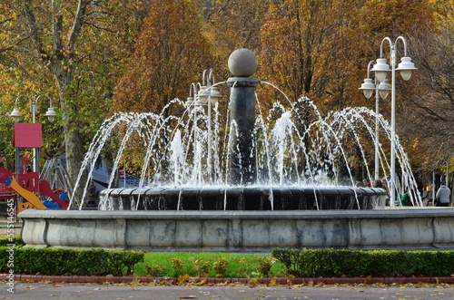 fuente con agua y detras parque infantil y arboles con hojas en Bilbao
