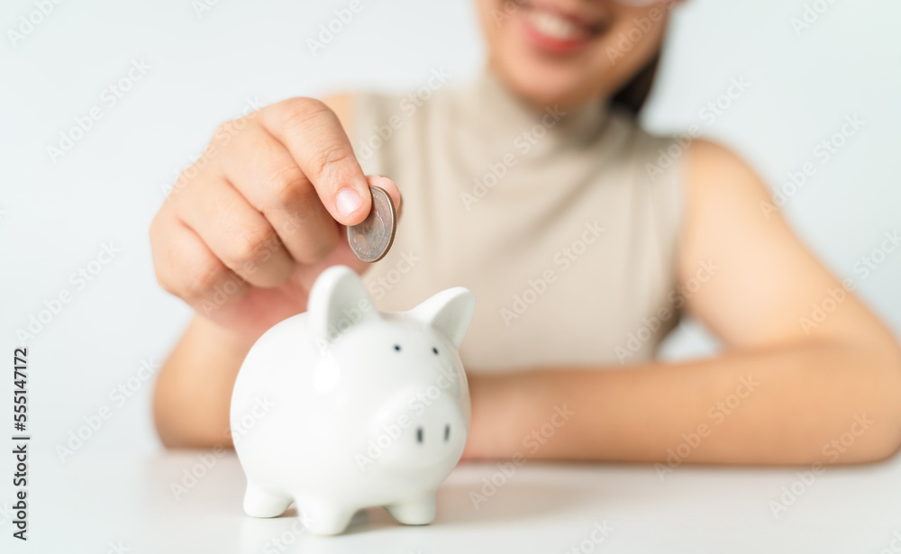 Close up of woman hand putting money coin into piggy bank for saving money. saving money and financial concept Close up of woman hand putting money coin into piggy bank for saving money. saving money and financial concept