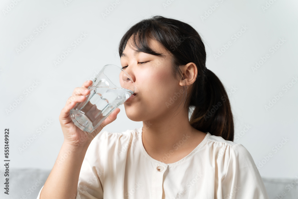 healthy beautiful young woman holding a glass of water drinking water sitting on the couch at the livingroom. healthy beautiful young woman holding a glass of water drinking water sitting on the couch at the livingroom.