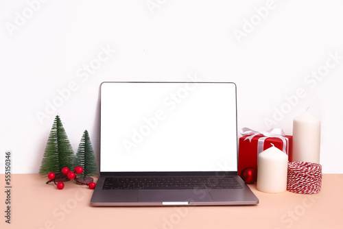 Blank screen on laptop for mock up. Christmas festival setup with gift boxes, candles, ribbons, jingle balls, Christmas tree. Mock up Christmas setup on white background. © Munchy Pixels