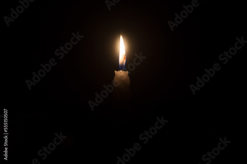 A single burning candle flame or light glowing on a beautiful spiral white candle on black or dark background on table in church for Christmas, funeral or memorial service with copy space