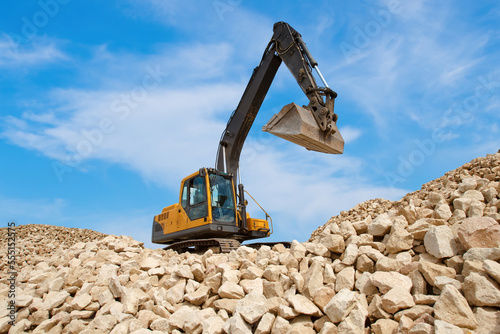 Development of stone quarry. Excavator on pile of stones. Crawler excavator under blue sky. Extraction of natural stone. Gravel loading excavator. Special equipment for extraction of gravel