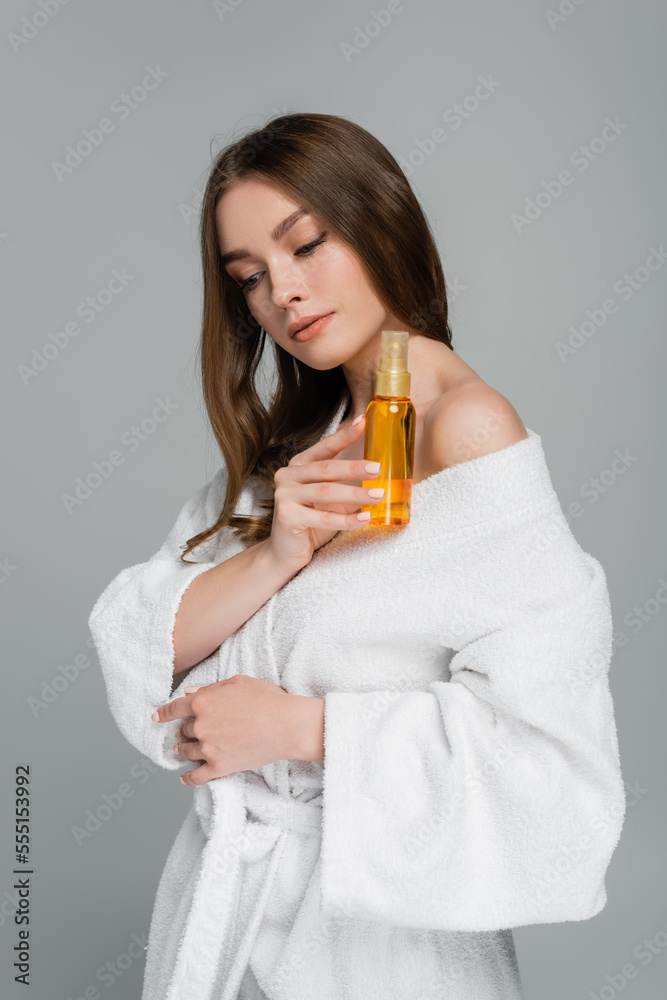 brunette young woman with shiny hair holding bottle with oil isolated on grey brunette young woman with shiny hair holding bottle with oil isolated on grey