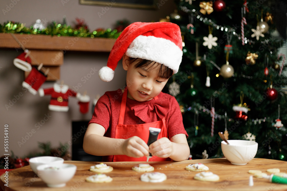 young girl wearing santa hat was preparing shortbread for Christmas party in front of Christmas tree at home young girl wearing santa hat was preparing shortbread for Christmas party in front of Christmas tree at home