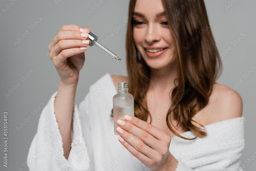 cheerful young woman with shiny hair holding bottle and pipette with serum isolated on grey cheerful young woman with shiny hair holding bottle and pipette with serum isolated on grey