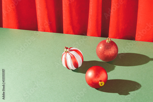 Vintage retro scene with red Christmas baubles on deep green table and red plush curtain. Creative xmas composition with copy spece.