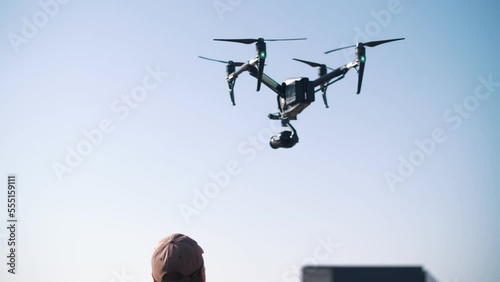 The drone flies against a background of blue sky and clouds, a view from below. The quadcopter with the camera hovers at a low altitude. Fast-rotating drone propellers.	 photo