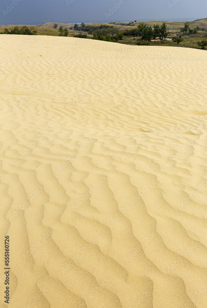 Sand dune ripples on large sand dune hill with rolling hills and dark blue sky in the background, Southeast of Leader; Saskatchewan, Canada Sand dune ripples on large sand dune hill with rolling hills and dark blue sky in the background, Southeast of Leader; Saskatchewan, Canada