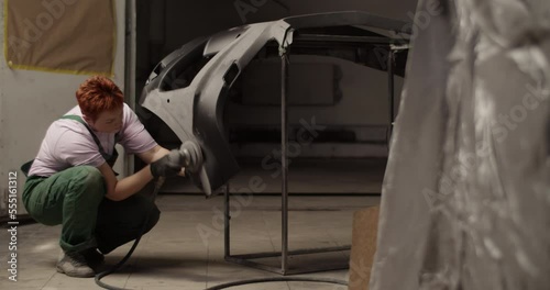 Female painter sanding bumper for priming