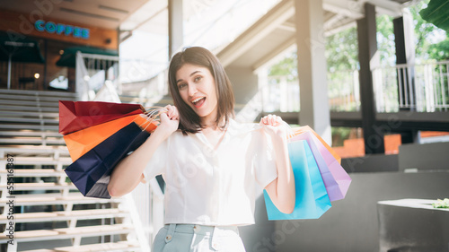 Woman smiling and holding a brightly colored shopping bag while walking through a shopping mall., Moments of happiness for ladies.