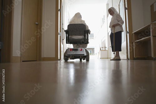 Rear view of a nun sitting in a motorized wheelchair with another nun standing beside her in a church photo