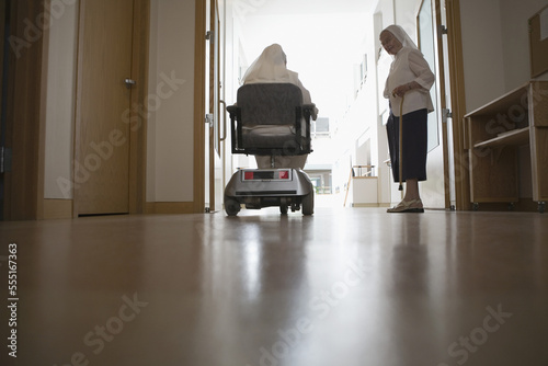 Rear view of a nun sitting in a motorized wheelchair with another nun standing beside her in a church