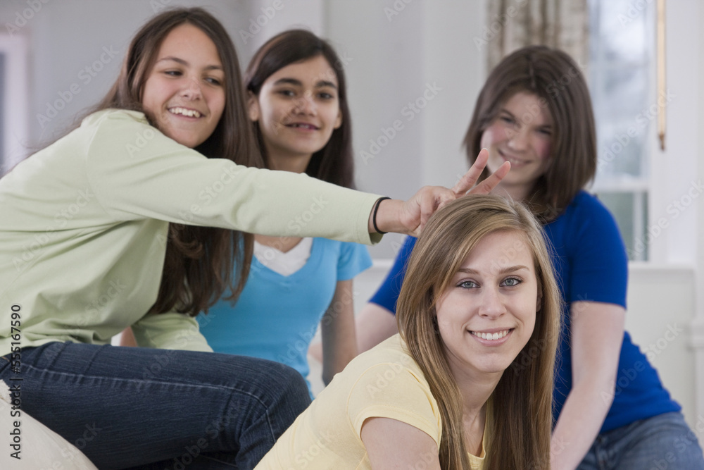 Portrait of four teenage girls sitting on a couch at home, one girl putting 'rabbit ears' behind the head of her friend in silliness Portrait of four teenage girls sitting on a couch at home, one girl putting 'rabbit ears' behind the head of her friend in silliness