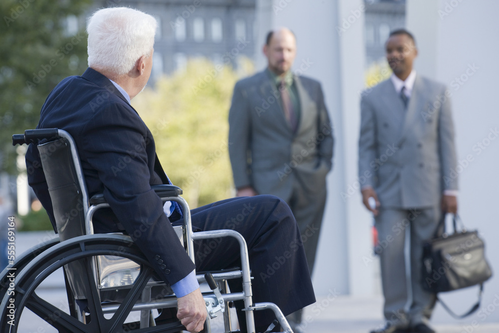 Smiling businessman on wheelchair, two colleagues in background Smiling businessman on wheelchair, two colleagues in background