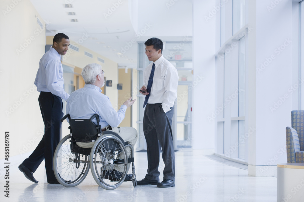 Three university professors talking in a corridor of a university, one with Muscular Dystrophy Three university professors talking in a corridor of a university, one with Muscular Dystrophy