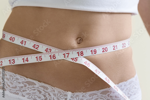 A young woman measuring her waist.