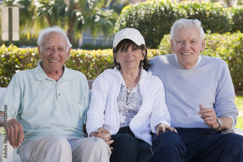 Three senior friends sitting on a park bench and smiling Three senior friends sitting on a park bench and smiling