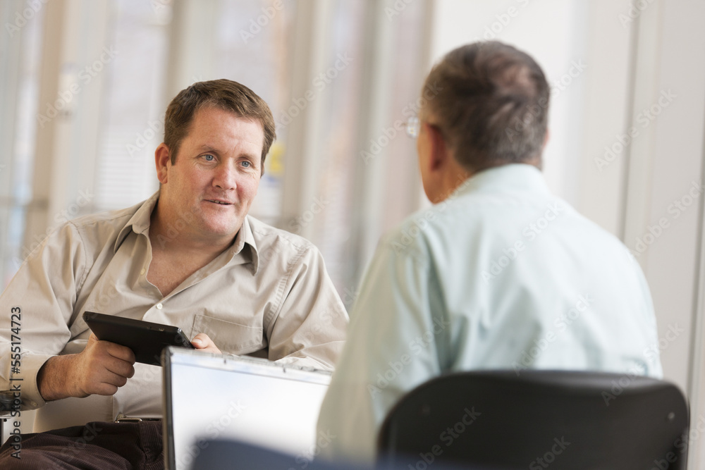 Man with spinal cord injury in wheelchair comparing a tablet with a laptop with his friend Man with spinal cord injury in wheelchair comparing a tablet with a laptop with his friend