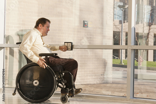 Businessman with spinal cord injury in wheelchair using automatic door opener at office building entrance photo
