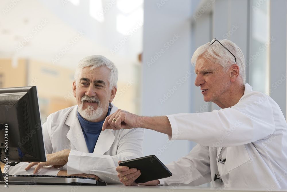 Two doctors discussing information on a computer and a tablet, one with Muscular Dystrophy Two doctors discussing information on a computer and a tablet, one with Muscular Dystrophy
