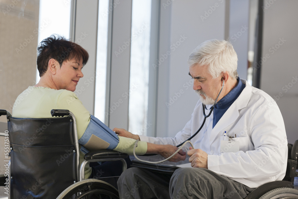 Doctor with muscular dystrophy in wheelchair checking the blood pressure of a patient Doctor with muscular dystrophy in wheelchair checking the blood pressure of a patient