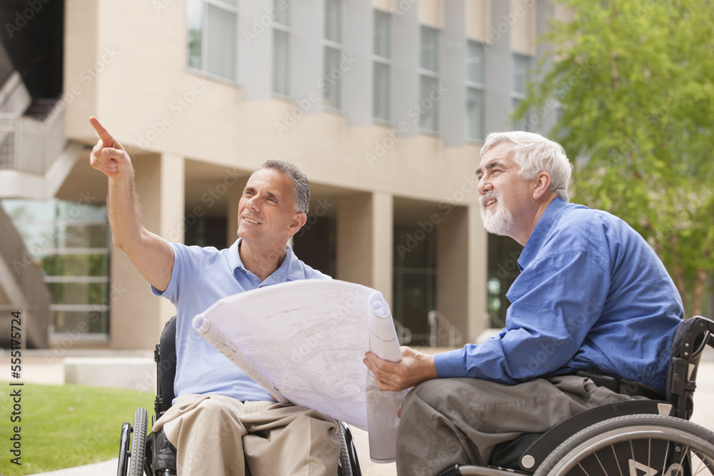 Design engineers reading Plans, one with muscular dystrophy and one with a spinal cord injury Design engineers reading Plans, one with muscular dystrophy and one with a spinal cord injury