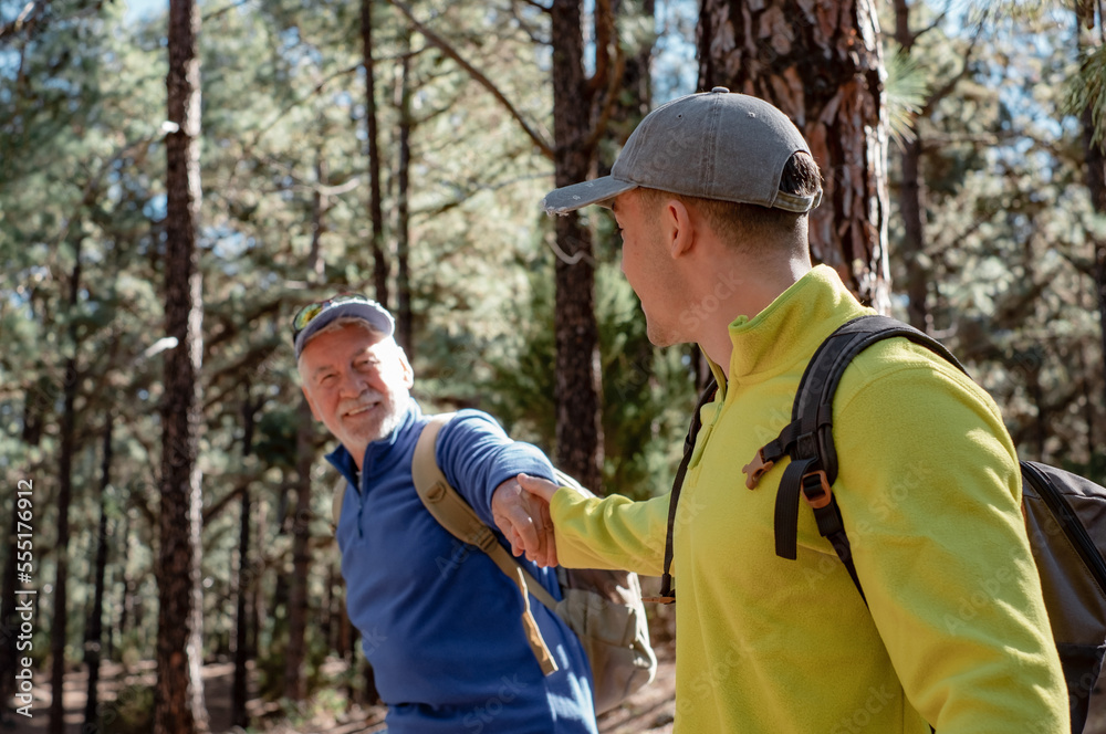 Fototapeta premium Happy and carefree couple of grandfather and teenager grandson hiking in the mountains sharing same passion for nature and healthy lifestyle together in the woods. Adventureisageless