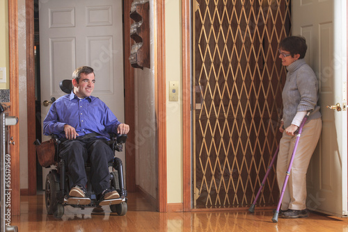 Woman with Cerebral Palsy helping man with Cerebral Palsy in motorized wheelchair into home elevator