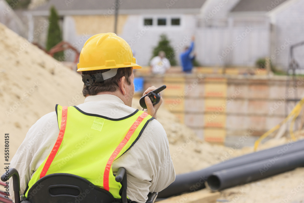 Construction supervisor with Spinal Cord Injury on walkie talkie with foundation and pipes in background Construction supervisor with Spinal Cord Injury on walkie talkie with foundation and pipes in background