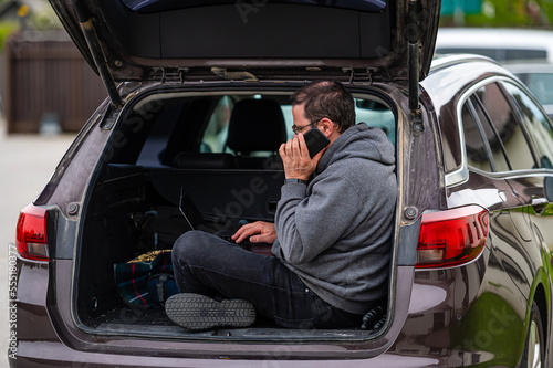 a man sitting in the open trunk of a car and working with a laptop, mobile technology, remote work