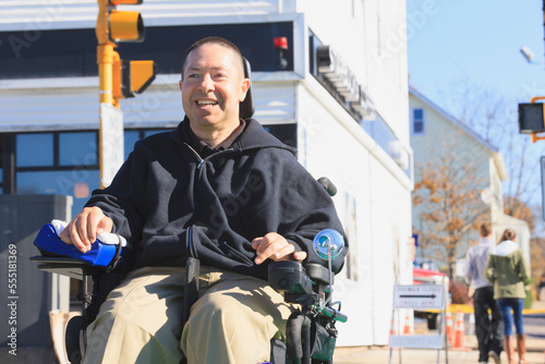 Man with spinal cord injury and arm with nerve damage in motorized wheelchair crossing public street while shopping