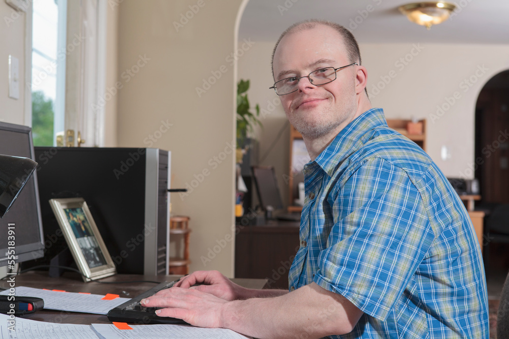 Man with Down Syndrome working at a computer in an office Man with Down Syndrome working at a computer in an office