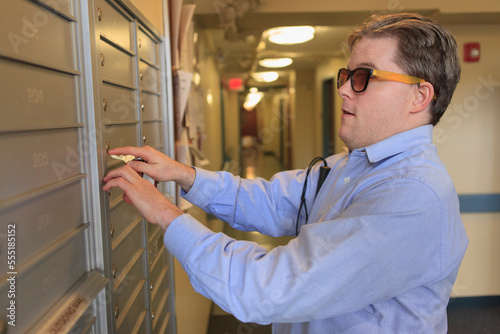 Man with congenital blindness opening his mailbox in his apartment building photo