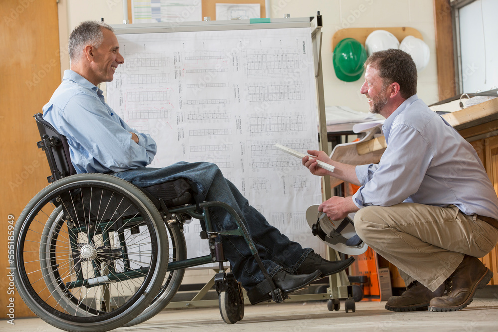 Two project engineers using a hanging rack for job site plans, one in a wheelchair with a Spinal Cord Injury