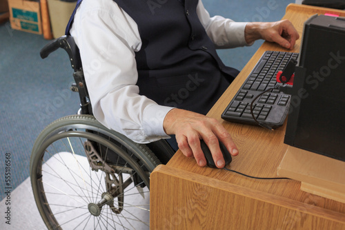 Man with Muscular Dystrophy in a wheelchair working at his computer in an office photo