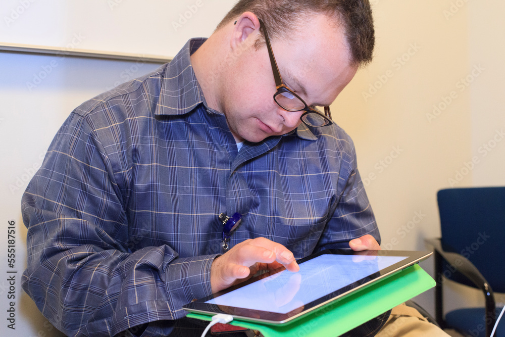 Hospital aid worker with Down Syndrome using a tablet in office Hospital aid worker with Down Syndrome using a tablet in office