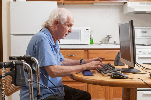 Man with Ataxia with his walker working on his computer in the kitchen photo