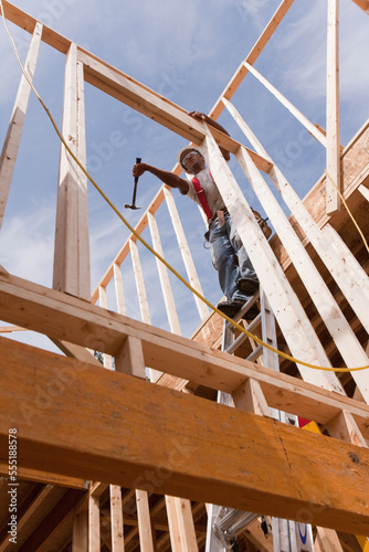 Carpenter using a hammer on the wall frame on the second floor of a house under construction photo