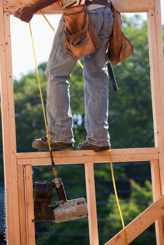 Carpenter pulling nail gun up to the second floor of a house under construction photo