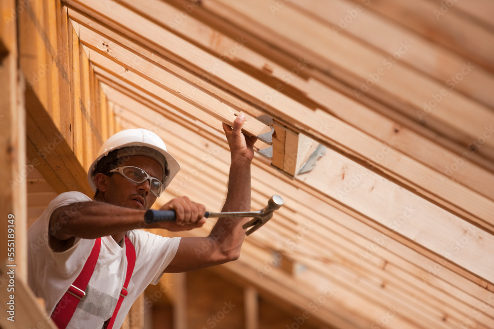 Hispanic carpenter hammering roof rafters at a house under construction Hispanic carpenter hammering roof rafters at a house under construction